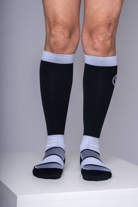 Person wearing black knee-high compression socks with white accents on a plain background
