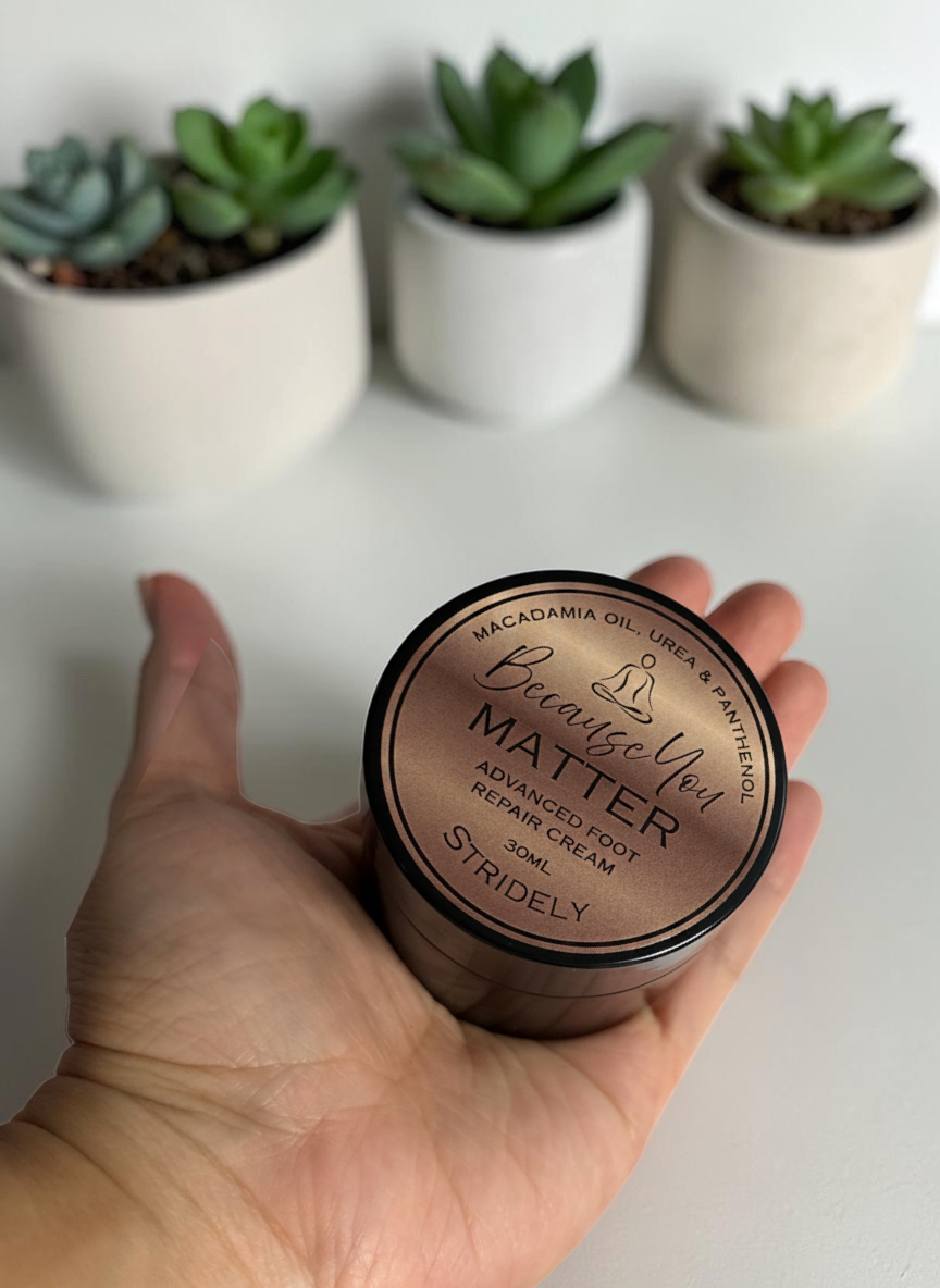 A hand holding a 30ml jar of STRIDELY advanced foot repair cream with a metallic bronze lid and black base.